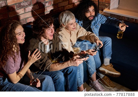 Diverse excited friends having fun by playing game console at home, indoors. Friendship, leasure, rest, home party concept Diverse excited friends having fun by playing game console at home, indoors. Friendship, leasure, rest, home party concept 77817888