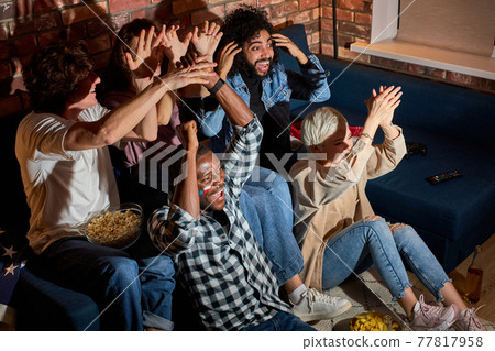 Young football fans gathered to cheer while watching football or other sport game at home Young football fans gathered to cheer while watching football or other sport game at home 77817958