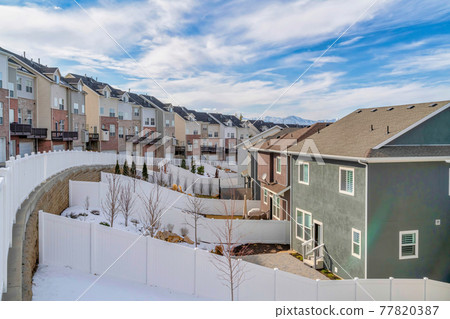 Snowy neighborhood landscape of home with backyards and townhouses along road 77820387