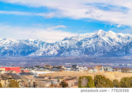Magnificent snowy Wasatch Mountain towering over a neighborhood and valley Magnificent snowy Wasatch Mountain towering over a neighborhood and valley 77820388