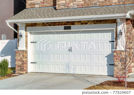 Home with driveway leading to hinged white garage door against stone brick wall Home with driveway leading to hinged white garage door against stone brick wall 77820607