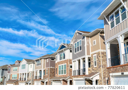 Row of beautiful houses on a peaceful neighborhood set against cloudy blue sky Row of beautiful houses on a peaceful neighborhood set against cloudy blue sky 77820611