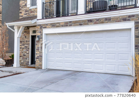 Front door of home besiden white garage door under balcony overlooking driveway Front door of home besiden white garage door under balcony overlooking driveway 77820640