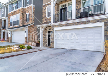 Houses with white garage doors under balcony with driveway and snowy yard views Houses with white garage doors under balcony with driveway and snowy yard views 77820641