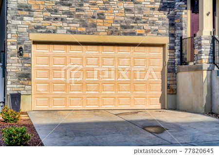 Wide panelled garage door of home with stone brick wall on a sunny neighborhood Wide panelled garage door of home with stone brick wall on a sunny neighborhood 77820645