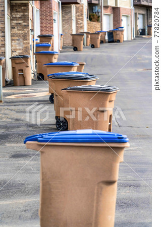 Grabage bins with wheels in front of townhouses along a paved neighborhood road 77820784