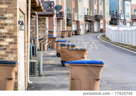 Garbage cans on road along townhouses with balconies and attached garages 77820785