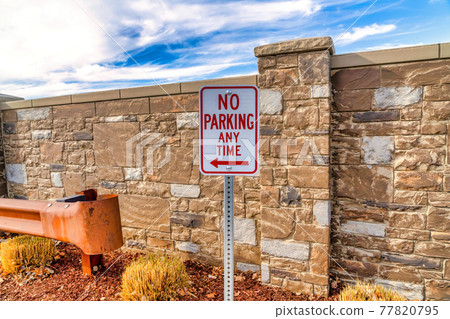 No Parking sign at a neighborhood with stone brick fence and blue sky background 77820795