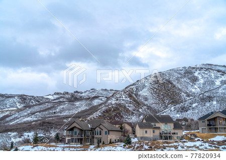 Homes nestled in the midst of snow dusted mountain slope viewed in winter Homes nestled in the midst of snow dusted mountain slope viewed in winter 77820934