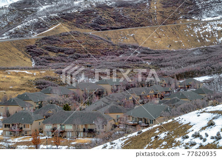 Group of houses sitting on a mountain terrain dusted with white snow in winter Group of houses sitting on a mountain terrain dusted with white snow in winter 77820935