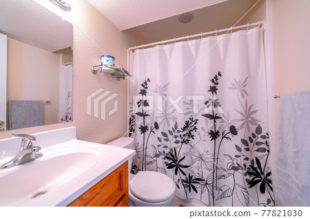 Interior of small bathroom with printed curtain on the bathtub and shower area 77821030