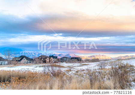 Sunset view of snowy valley in winter with homes against sunlit frosted mountain 77821116