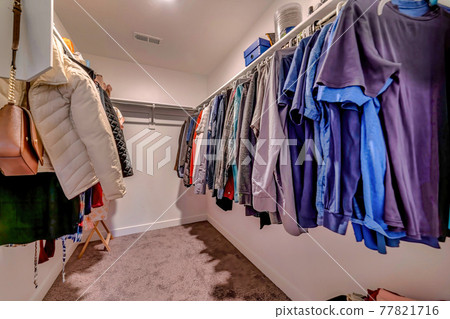 Walk in closet interior with clothes hanging on metal rods below wall shelves 77821716