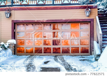 Panelled metal garage door of home beside stairs that leads up to snowy balcony 77822571