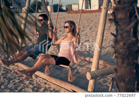 Young attractive couple swinging on seesaw on the beach. 77822697