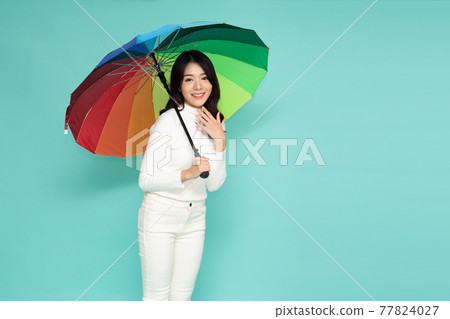 Young happy Asian woman holding colorful umbrella isolated on green background Young happy Asian woman holding colorful umbrella isolated on green background 77824027