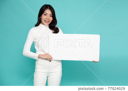 Young asian woman showing and holding blank white billboard isolated on green background Young asian woman showing and holding blank white billboard isolated on green background 77824029