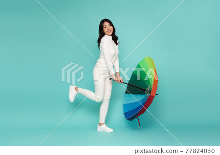 Young happy Asian woman holding colorful umbrella isolated on green background Young happy Asian woman holding colorful umbrella isolated on green background 77824030