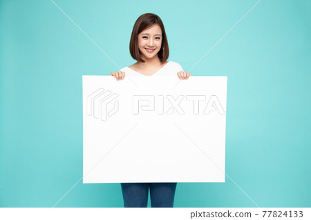 Young asian woman showing and holding blank white billboard isolated on green background Young asian woman showing and holding blank white billboard isolated on green background 77824133