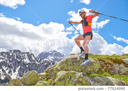 Man athlete jumps between the stones during a trail workout in the mountains Man athlete jumps between the stones during a trail workout in the mountains 77824998