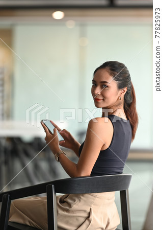 A beautiful woman is using a mobile phone while sitting in office. A beautiful woman is using a mobile phone while sitting in office. 77825973