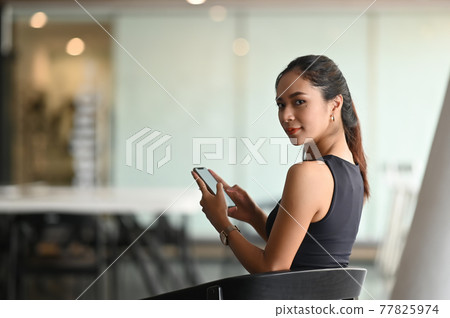 A beautiful woman is using a mobile phone while sitting in office. 77825974