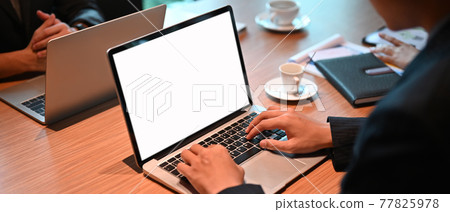 An office man is using a computer laptop with a white blank screen at the wooden working desk. An office man is using a computer laptop with a white blank screen at the wooden working desk. 77825978