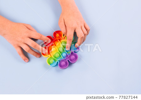 Close up of boy's hands using rainbow pop it fidget toy on blue background with copy space. Push bubble fidget sensory toy - washable and reusable silicone stress relief toy. Selective focus Close up of boy's hands using rainbow pop it fidget toy on blue background with copy space. Push bubble fidget sensory toy - washable and reusable silicone stress relief toy. Selective focus 77827144