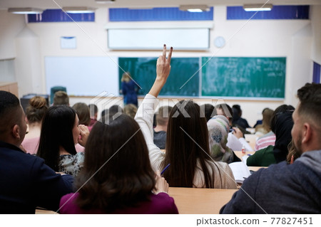 female student sitting in the class and raising hand up 77827451