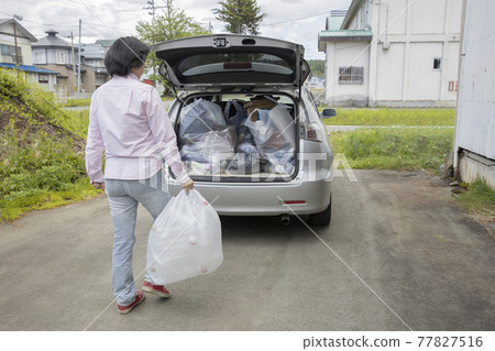 A woman who puts household waste in a car A woman who puts household waste in a car 77827516