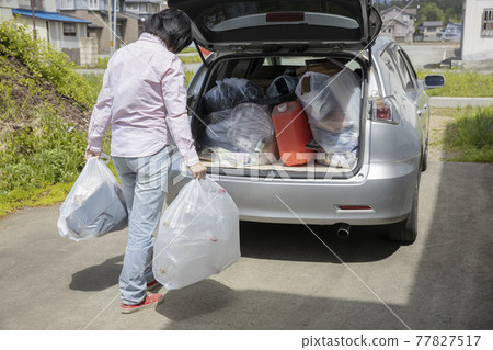 A woman who puts household waste in a car 77827517