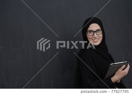 Young Arab businesswoman in traditional clothes or abaya holding tablet computer 77827795