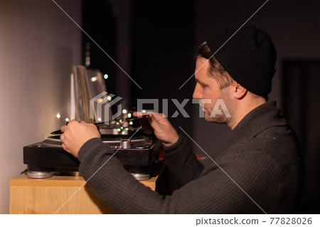 Young unshaven handsome millennial guy puts record on turntable 77828026
