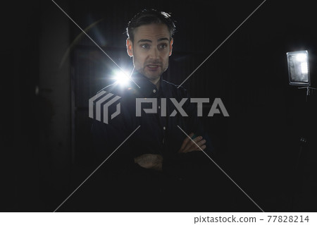 An influencer, artist and musician, dress with black shirt, poses for the camera in one of his photographic shootings for social networks, in a dark backstage area, at night, in Spain. An influencer, artist and musician, dress with black shirt, poses for the camera in one of his photographic shootings for social networks, in a dark backstage area, at night, in Spain. 77828214
