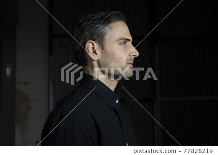An influencer, artist and musician, dress with black shirt, poses for the camera in one of his photographic shootings for social networks, in a dark backstage area, at night, in Spain. An influencer, artist and musician, dress with black shirt, poses for the camera in one of his photographic shootings for social networks, in a dark backstage area, at night, in Spain. 77828219
