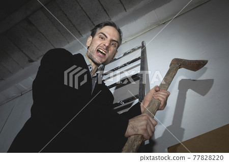 A psychopathic madman, young adult, threatens with an old and rusty ax in his hands, while he remains perched on a ladder, ready to attack with a violent expression. Spain. A psychopathic madman, young adult, threatens with an old and rusty ax in his hands, while he remains perched on a ladder, ready to attack with a violent expression. Spain. 77828220
