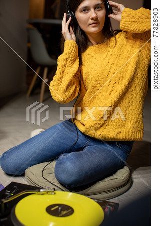 girl sitting on floor enjoys to music with headphones and analog turntable girl sitting on floor enjoys to music with headphones and analog turntable 77828903