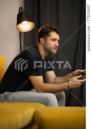 Crazy obsessed with games guy plays video game holding console gamepad in hands Crazy obsessed with games guy plays video game holding console gamepad in hands 77828907