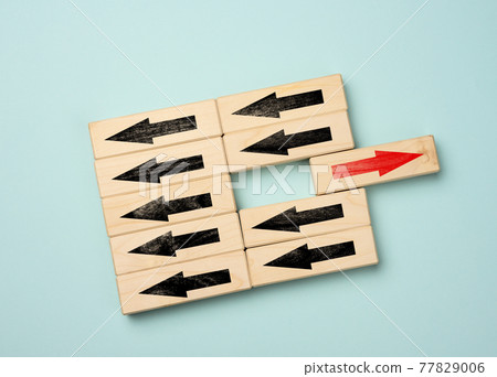 wooden cubes with black arrows in one direction and one block with a red arrow in the opposite direction. Concept of difference, uniqueness wooden cubes with black arrows in one direction and one block with a red arrow in the opposite direction. Concept of difference, uniqueness 77829006