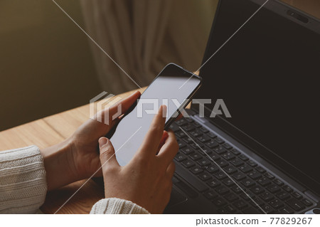 Photograph of the desk and the hands of a young woman, checking the mobile phone, smartphone, early in the morning, while teleworking at home, in Madrid, Spain. Photograph of the desk and the hands of a young woman, checking the mobile phone, smartphone, early in the morning, while teleworking at home, in Madrid, Spain. 77829267