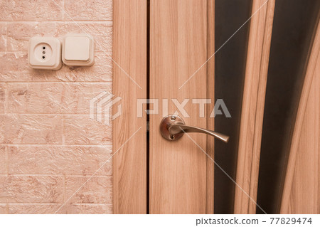 Part of the interior of a modern living room with an iron doorknob, socket and light switch close-up Part of the interior of a modern living room with an iron doorknob, socket and light switch close-up 77829474