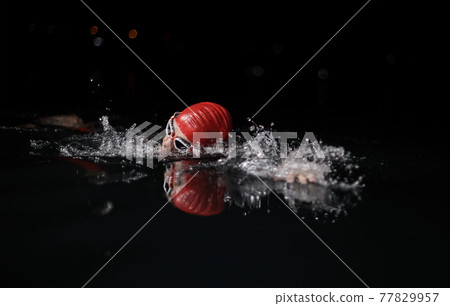 triathlon athlete swimming in dark night wearing wetsuit 77829957