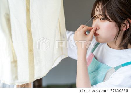 A woman who smells a shirt that is dried indoors 77830286