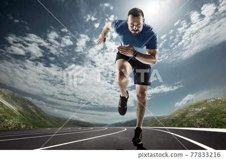 Professional male runner, jogger on road and sky background. Caucasian fit athlete practicing, training excited 77833216