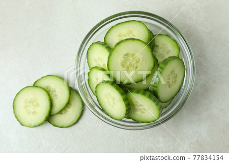Bowl with cucumber slices on white textured background 77834154