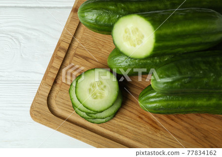 Board with ripe cucumbers on white wooden table 77834162