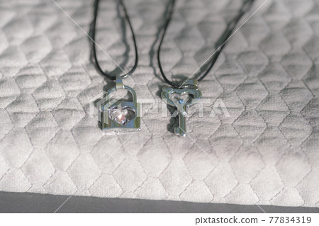Couple set pendant necklace with a key and a lock for lovers shoot outdoors in a sunny day closeup. Selective focus Couple set pendant necklace with a key and a lock for lovers shoot outdoors in a sunny day closeup. Selective focus 77834319