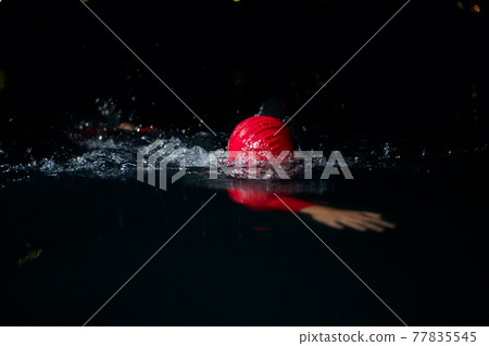 triathlon athlete swimming in dark night wearing wetsuit 77835545