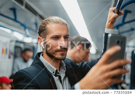 attractive man using his smartphone in subway train . 77835884
