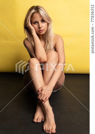 A girl sitting on the floor with her feet cross-legged keeps her head on a beautiful yellow background cheerful girl, beautiful body skin perfect, sunglasses. erotic lifestyle, healthy soppy 77836352